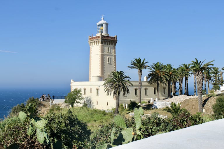 A scenic view of Cape Spartel Lighthouse surrounded by lush palm trees on a sunny day in Morocco.