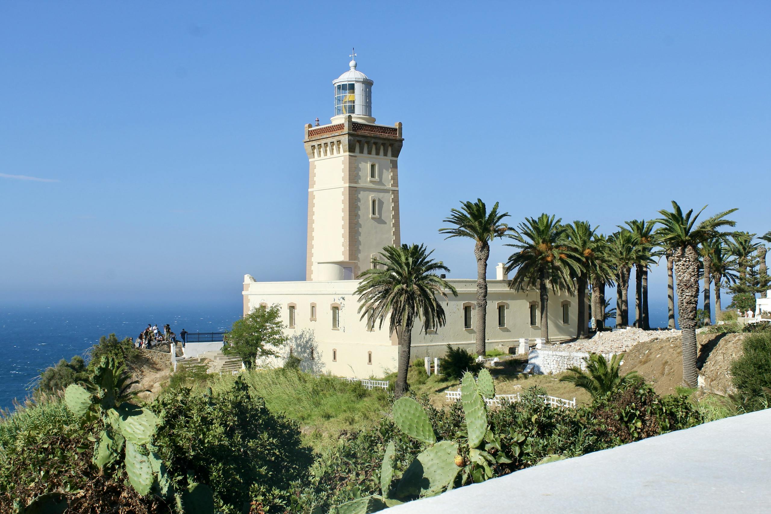 A scenic view of Cape Spartel Lighthouse surrounded by lush palm trees on a sunny day in Morocco.