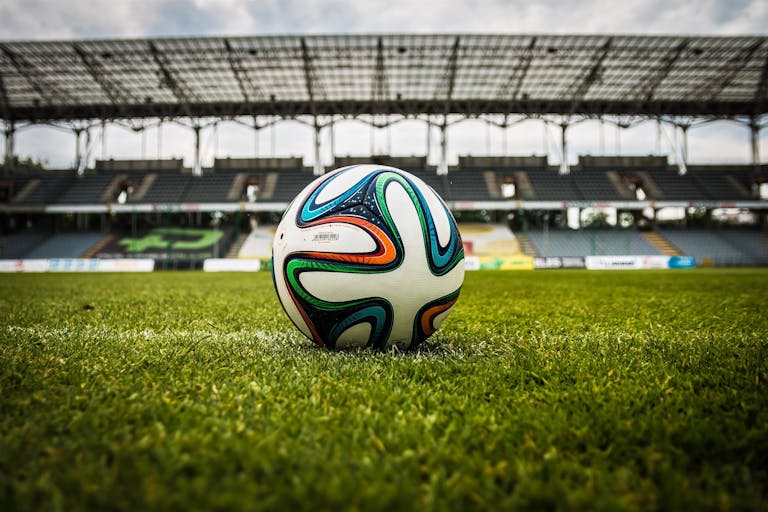 A vibrant soccer ball rests on a lush green field inside an empty stadium, capturing the essence of sports.